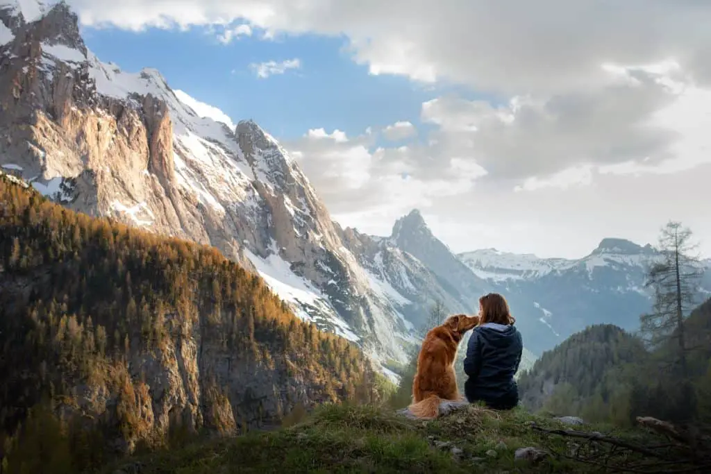 a woman sitting next to her dog during a hike